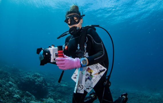 under the ocean, scuba diver holds waterproof camera